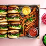 Åtta hamburgare med formbarfärs, sötpotatispommes och skålar med röror och picklad rödlök