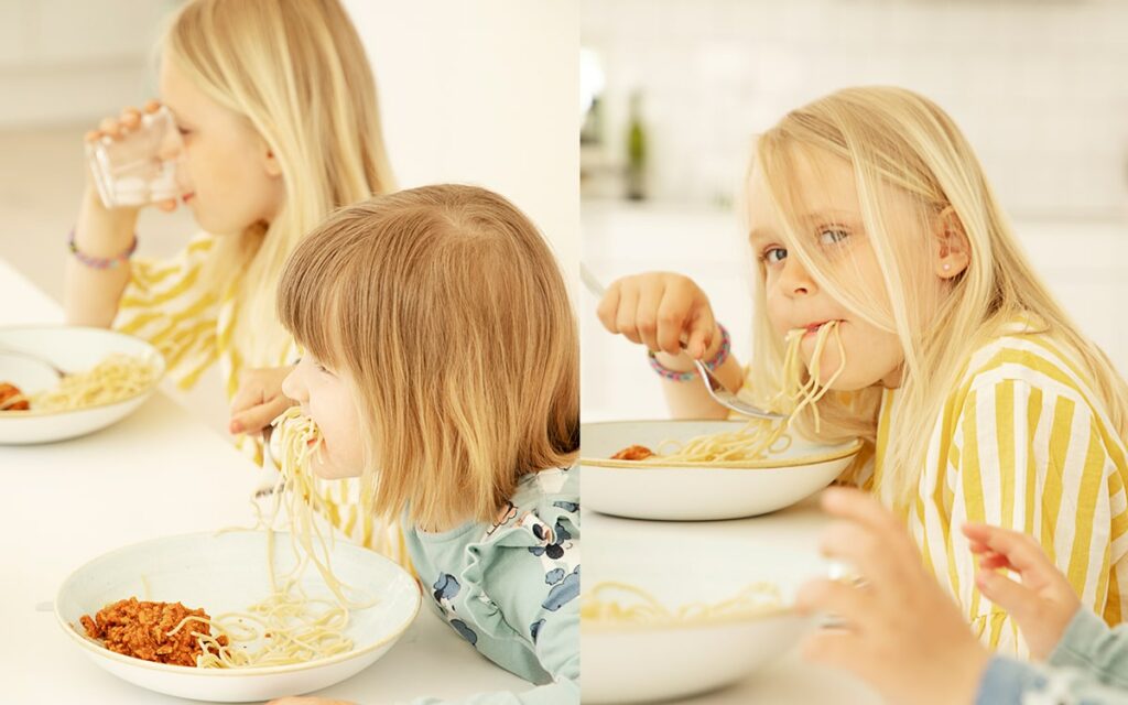 Två barn äter vego bolognese vid köksbord.