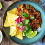 En tallrik med chili sin carne gjord på Baljväxtfärs toppad med picklad rödlök, nachochips och färsk koriander.