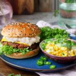 Vegetarisk cheeseburgare med karamelliserad lökdressing och sallad, en skål med chlli cheese majs och koriander.